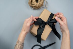pexels-photo-3927233-3927233 Close-up of hands wrapping a gift box with a black ribbon, ready for gifting.